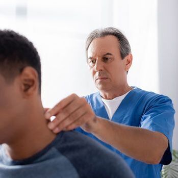 Lékař provádí diagnostické vyšetření pacienta s bolestí krku.